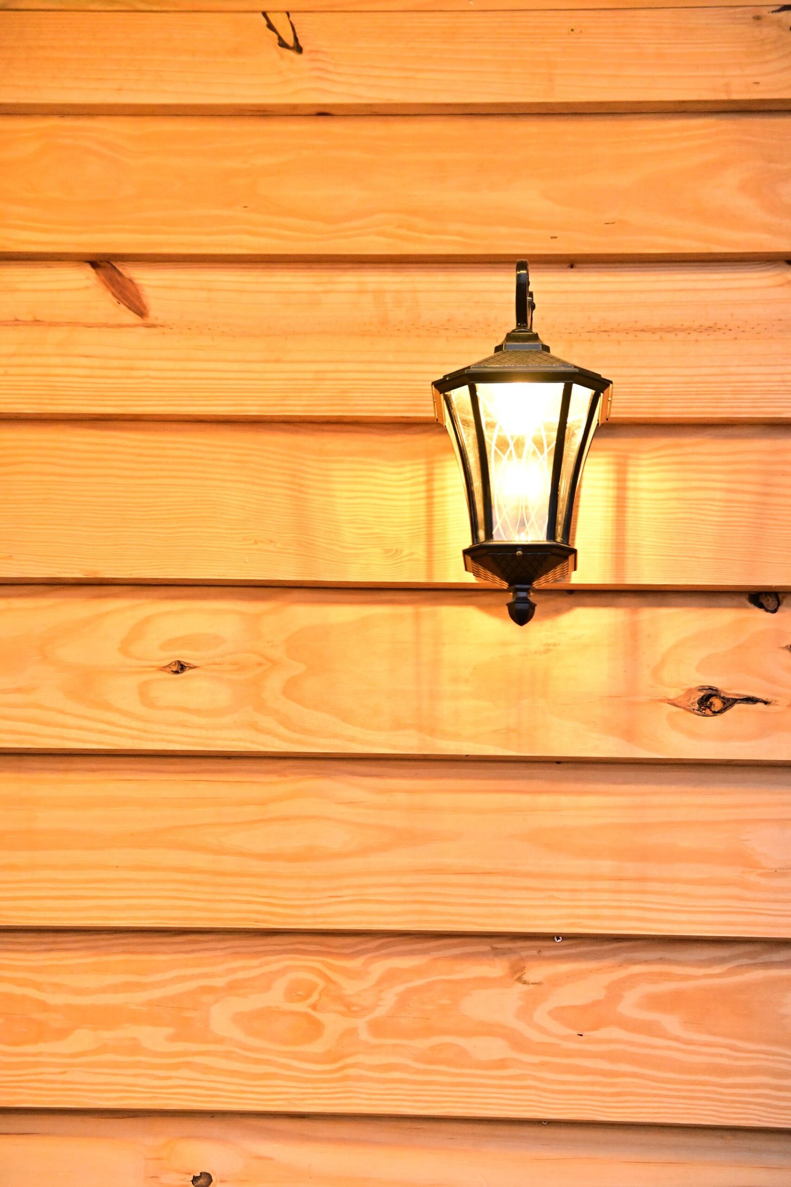 A warm-lit wall lantern mounted on a polished wooden siding creates an inviting ambiance.